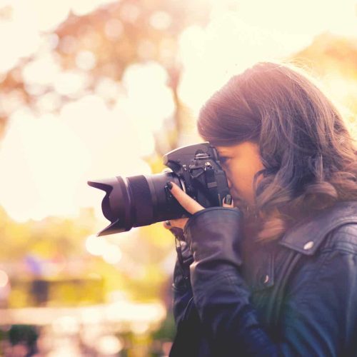 attractive young woman photographer taking pictures with professional digital camera outside. vintage effect